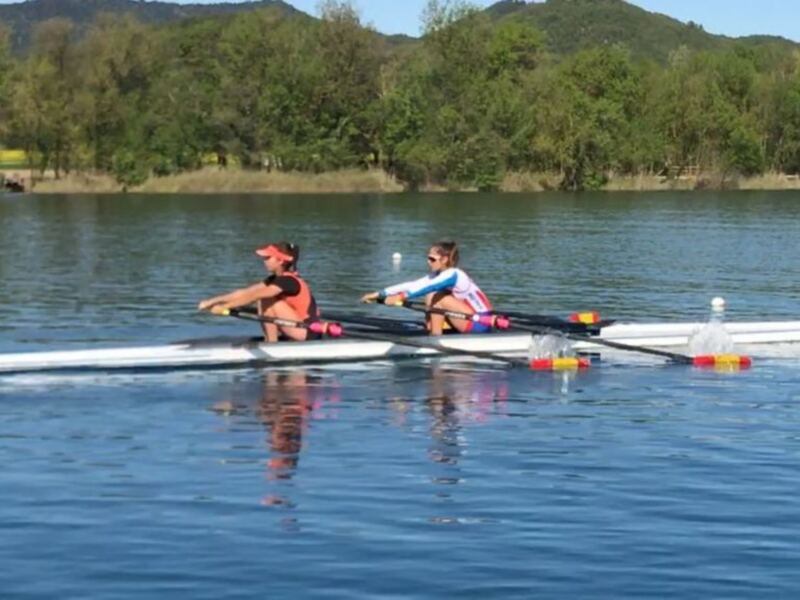 Dos personas remando en una canoa en un lago con árboles y montañas en el fondo.