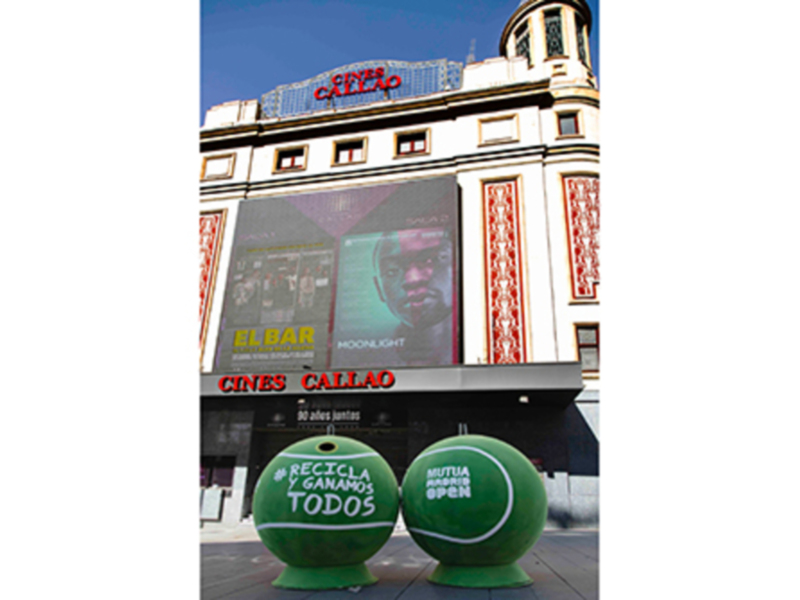 Exterior of Cines Callao movie theater with large advertisement and green spherical decorations promoting recycling.