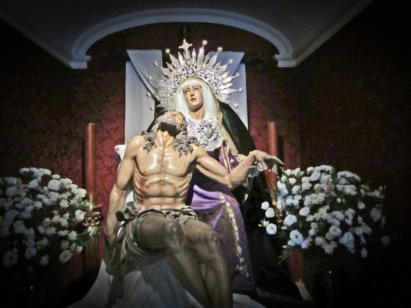 Estatua de Cristo y Virgen en una capilla con flores y velas