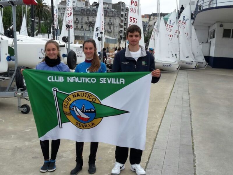 Equipo del Club Náutico Sevilla posando con su bandera en un puerto de veleros.