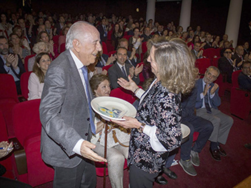 Un hombre y una mujer intercambian un obsequio en un auditorio lleno de espectadores que aplauden.