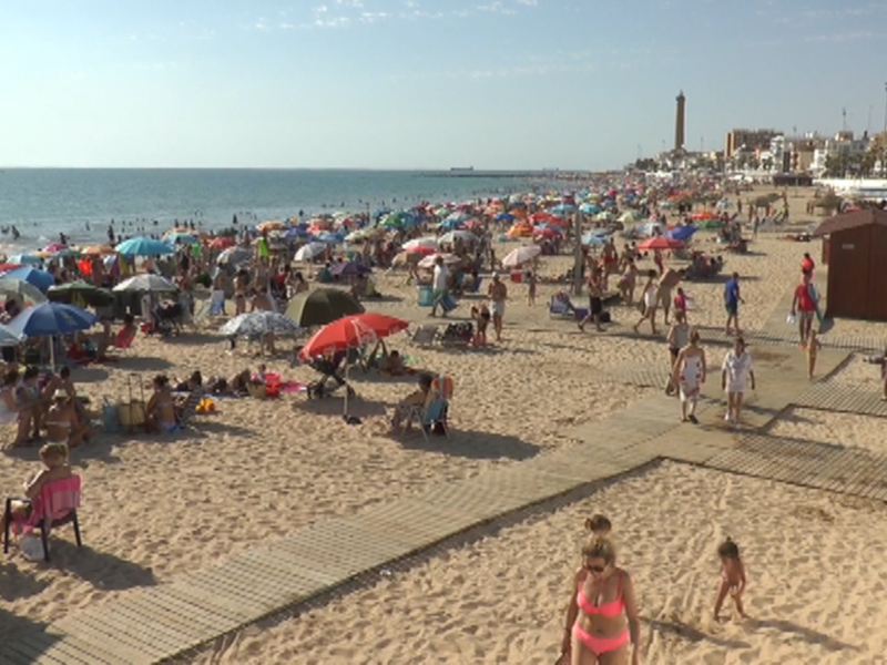 Playa de la Malagueta, Málaga, con multitud de bañistas bajo sombrillas y en la arena bajo un cielo despejado.
