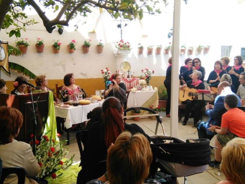 Un grupo de personas disfrutando de una comida en un ambiente festivo, con mesas decoradas con flores y una bandera en la pared.