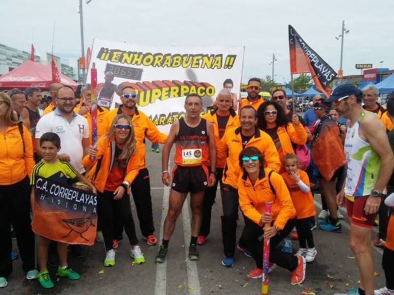 Equipo de atletas y voluntarios celebrando el maratón con pancarta y banderas de color naranja.