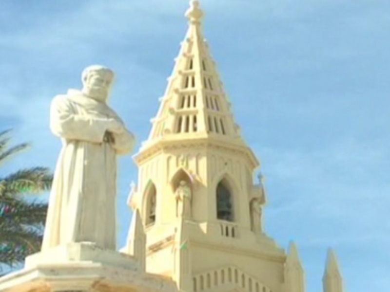 Estatua de San Francisco de Asís frente a la catedral de Malta bajo un cielo azul claro.