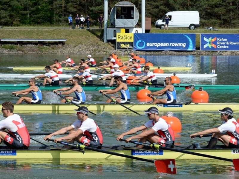 Rowers competing in a rowing event, with a banner reading 'European Rowing' and 'Kefue River & Rowing Centre' in the background.