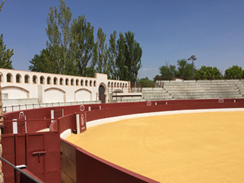Plaza de toros vacía con arena amarilla y arquitectura clásica bajo un cielo azul claro.