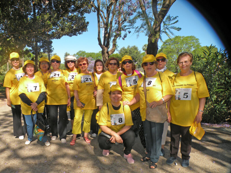 Una grupo de personas vestidas de amarillo y con número 21 en la camiseta, posando en un parque con árboles y flores. La imagen muestra un ambiente de equipo y camaradería.