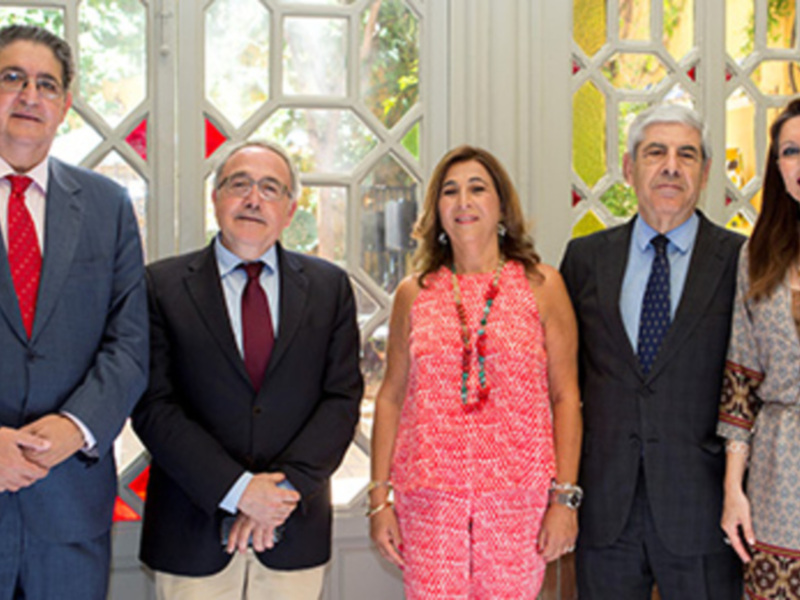 Grupo de personas posando frente a una puerta de cristal con un diseño floral, posiblemente en un evento formal o de negocios.