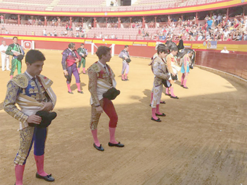 Toro de lidia en plaza de toros con matadores y público en el fondo.