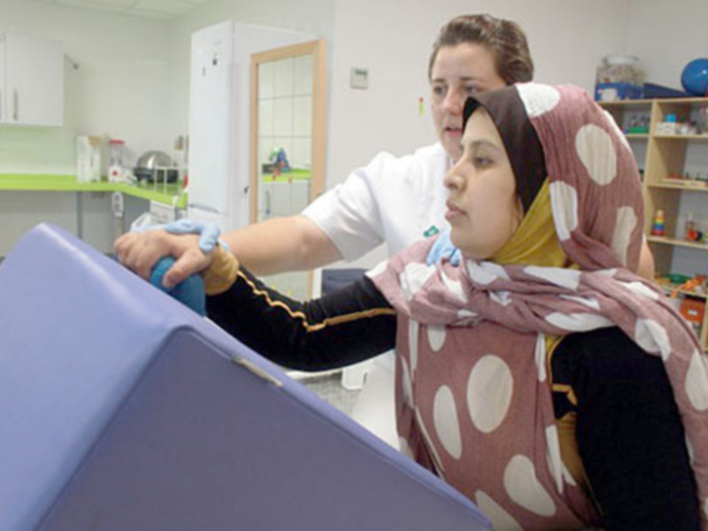 Una mujer con un hijab ayuda a una persona a usar un ordenador en un entorno de oficina o centro de atención al público.