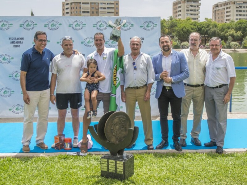 Celebración de la Federación Andaluza de Remo con miembros y trofeo en un entorno acuático.