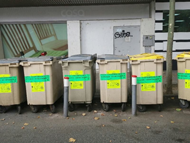Contenedores de reciclaje y basura en fila junto a un edificio.