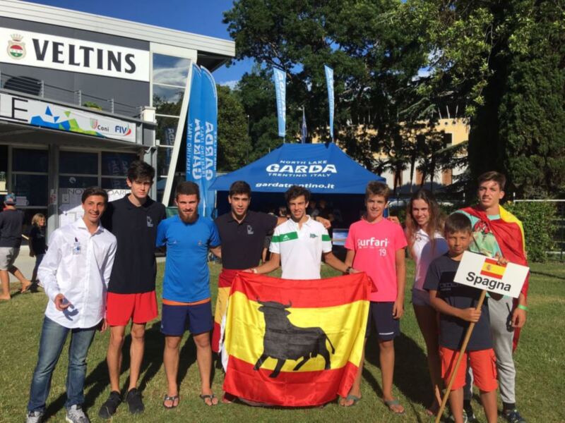 Equipo español posando con bandera y banderín en evento deportivo en Garda, Italia.