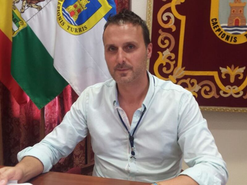 Un hombre en una oficina formal, con una bandera y un escudo en el fondo.
