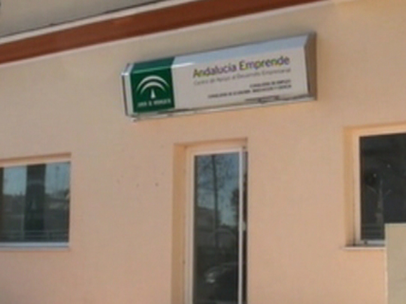 Placa de identificación de la empresa Andalucía Emprende en una pared de color beige con dos ventanas laterales.