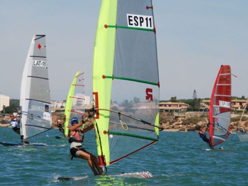 Competición de vela de viento en el mar, con veleros de diferentes banderas navegando juntos.