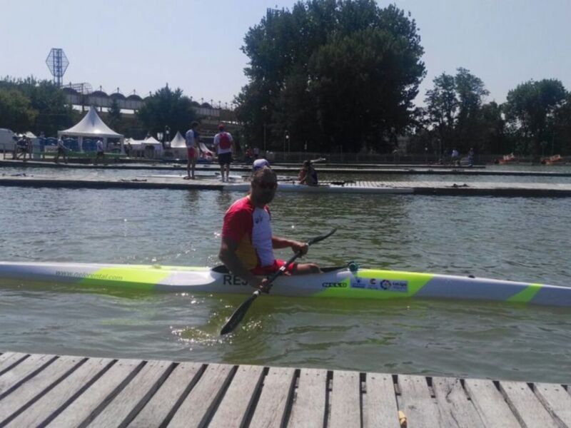Un competidor en canoa realiza una maniobra en un lago con un entorno de actividades acuáticas al fondo.