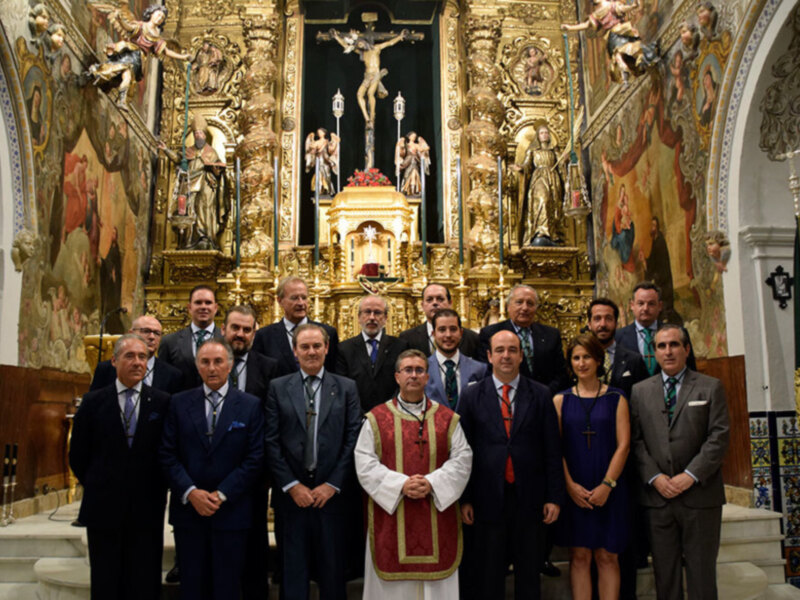 Grupo de personas posando en una iglesia, con un altar dorado y estatuas religiosas en el fondo.