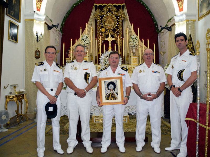 Oficiales en uniforme blanco posan con un retrato enmarcado en una iglesia decorada con velas y flores.