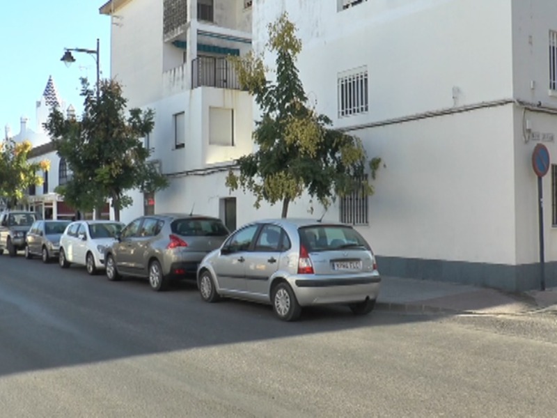 Un pequeño coche aparcado en la acera de una calle en un día soleado, con árboles y edificios blancos al fondo.