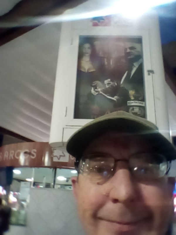 Retrato de hombre con gorra y gafas, reflejado en una ventana con imagen de arte en el fondo.