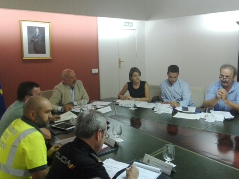 Un grupo de personas se reúne en una sala de conferencias, con una bandera de la UE y la bandera española en el fondo. Los participantes están sentados alrededor de una mesa con documentos y lápices. El ambiente parece ser formal y profesional.