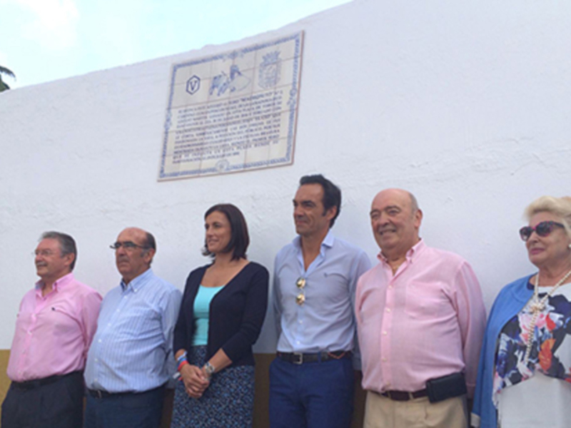 Un grupo de personas posa junto a una placa conmemorativa en una pared blanca.