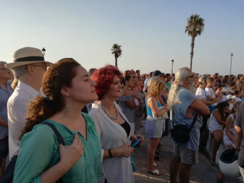 Gente disfrutando de un evento al aire libre en un lugar con palmeras y un cielo claro.