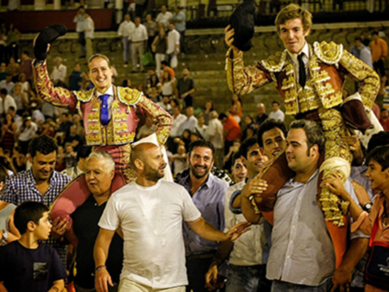 Un torero celebrando su triunfo en un espectacular evento taurino, rodeado por una multitud entusiasta en un estadio lleno de asistentes.