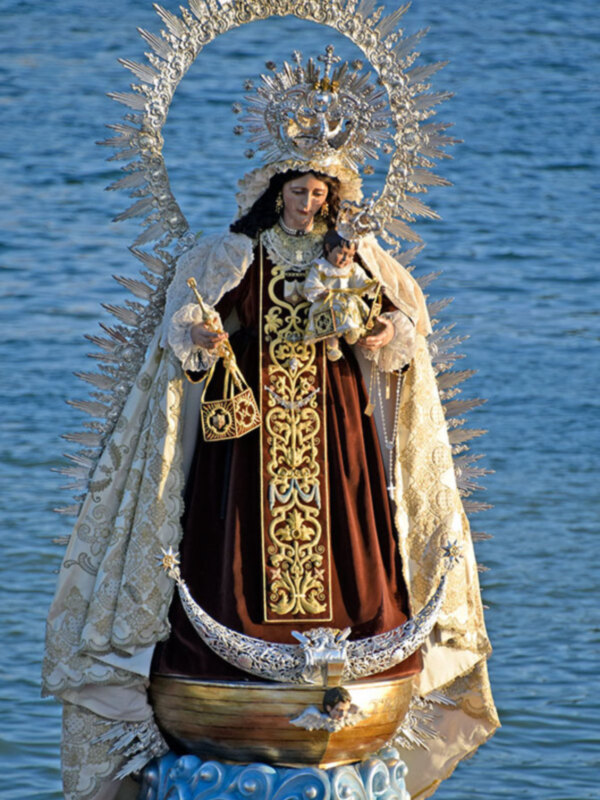 Figura religiosa con vestimentas ornamentales y corona, frente a un fondo de agua.