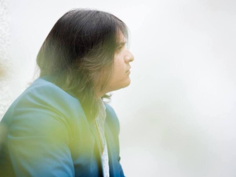 Persona con cabello largo y suave, vistiendo una chaqueta azul, mirando hacia el horizonte en un entorno suave y desenfocado.