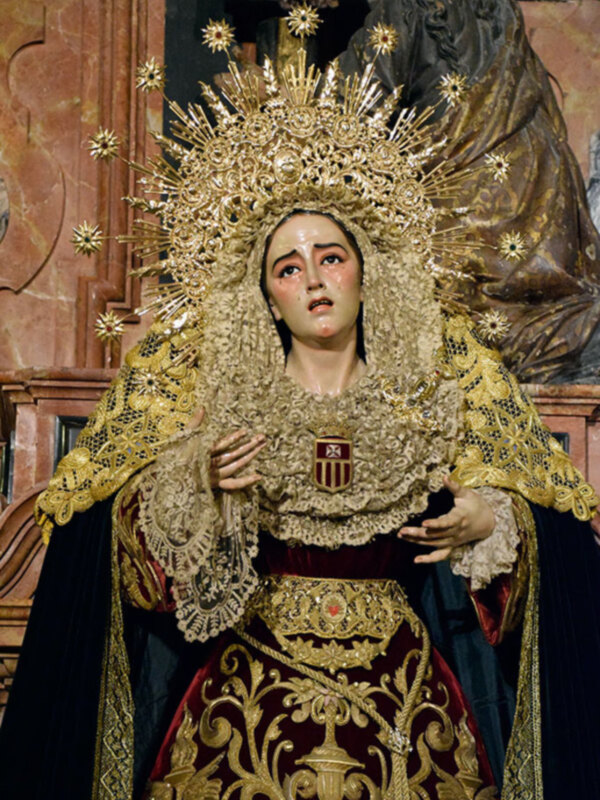 Imponente imagen de la Virgen María con traje y corona dorada, representando solemnidad y devoción.