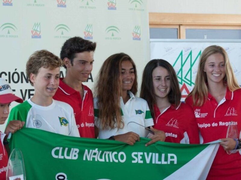 Un equipo de regata posando con su bandera en un evento deportivo en Sevilla.