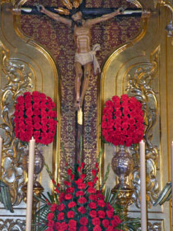 Cristo en la cruz con flores rojas y decoración dorada en un altar religioso.