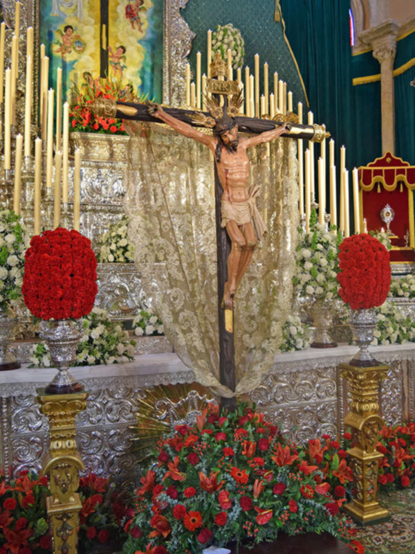 Crucifijo en un altar adornado con flores y velas, en una iglesia.