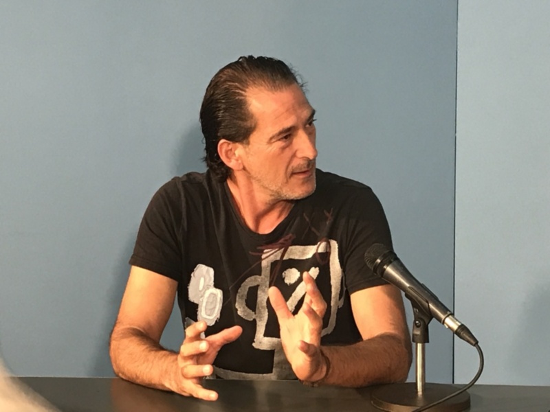 Hombre hablando en una mesa con micrófono, expresando con gestos.