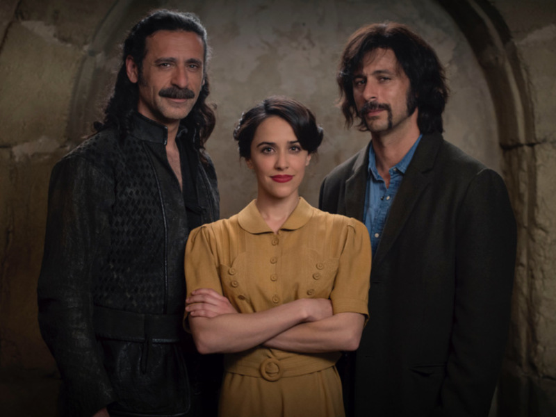 Tres personajes en un entorno medieval, con vestimentas que sugieren un pasado histórico.