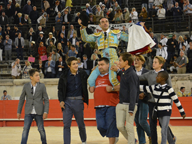 Un torero celebra con un mantón en un espectáculo taurino, rodeado por espectadores en un anfiteatro.
