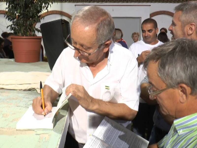 Un hombre en blanco escribe en un papel mientras otros lo observan.