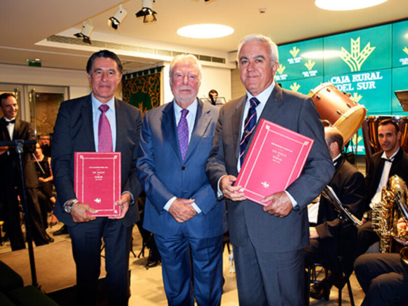 Tres hombres en trajes formales sostienen certificados rojos en una ceremonia formal en CAIA Rural del Sur.