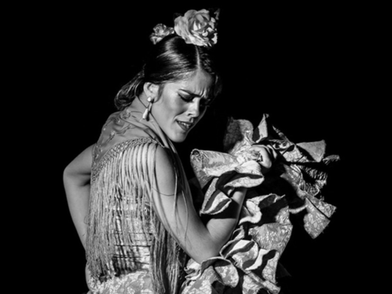 Actriz en traje de flamenco con flores en el cabello, expresión dramática en escena.