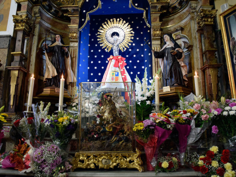 Altar con estatuas religiosas, flores y velas en un entorno eclesiástico.
