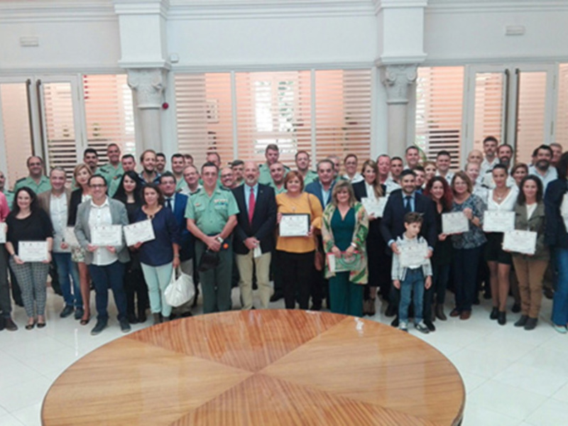 Grupo de personas posando con certificados en una sala con ventanas y columnas clásicas.