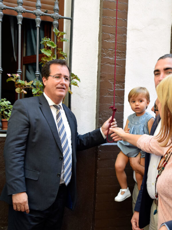 Un hombre en traje y corbata intercambia una cuerda con una niña y una mujer en un entorno urbano.
