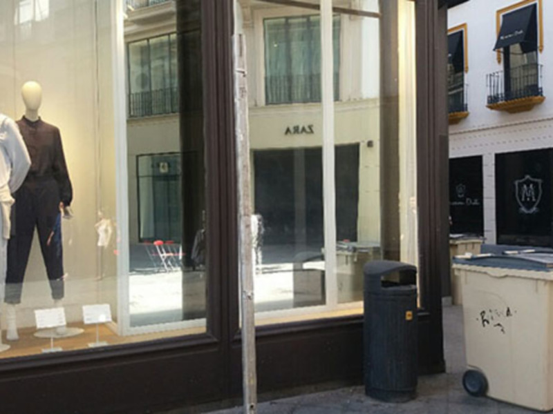 Tienda de ropa con maniquíes en la ventana, reflejando edificios vecinos.