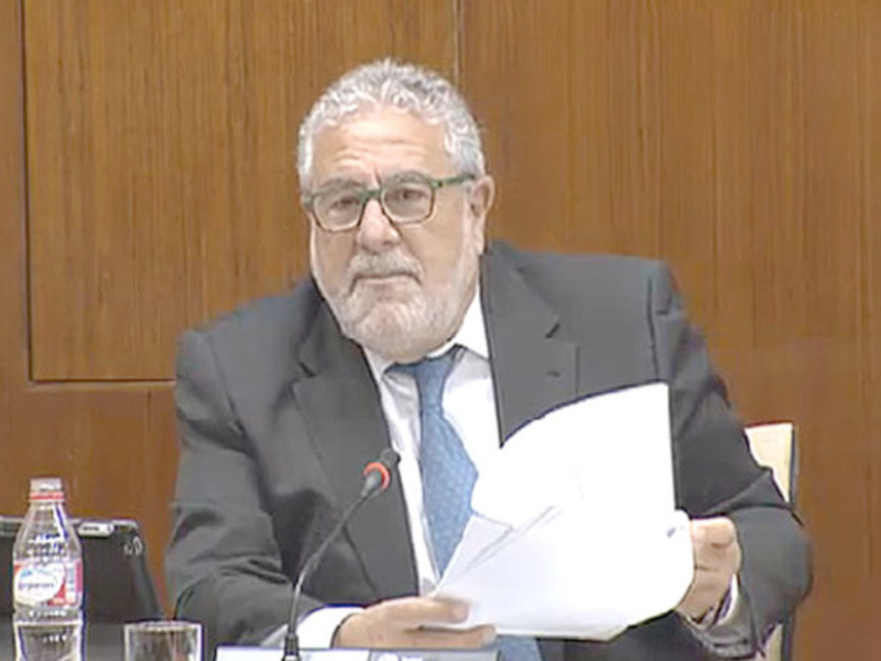 Un hombre en traje y corbata, sosteniendo un documento mientras se encuentra en una sala de conferencias con paredes de madera.