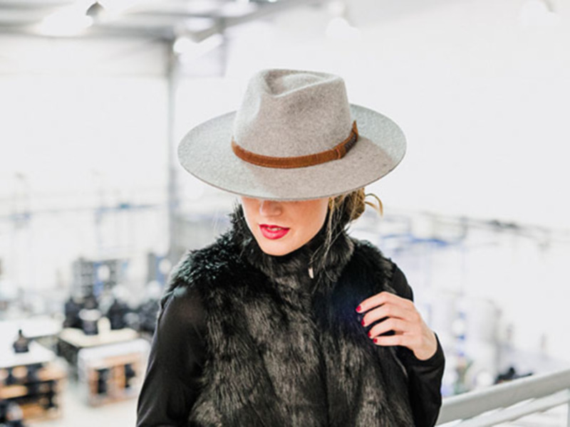 Moda invierno: mujer con sombrero de fieltro y abrigo de pelaje en un entorno industrial.