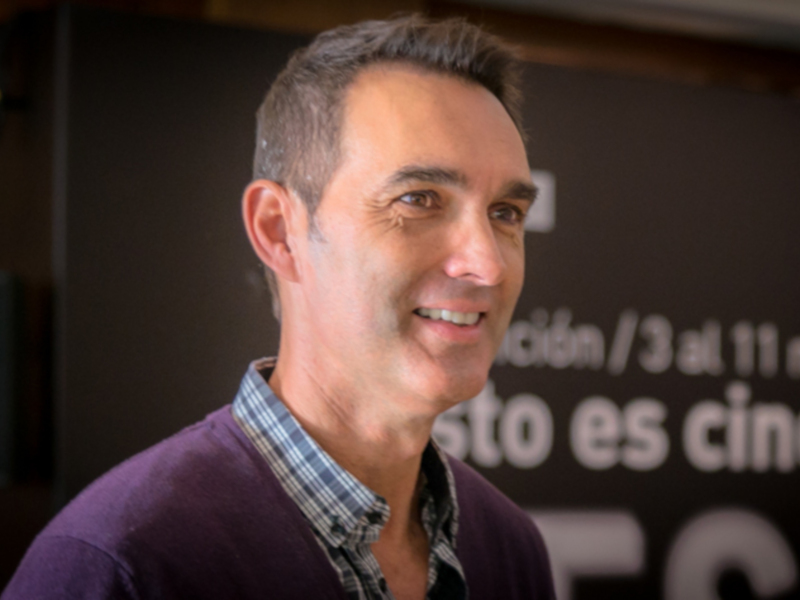 Retrato de hombre sonriente en evento de cine, fondo con texto en español.