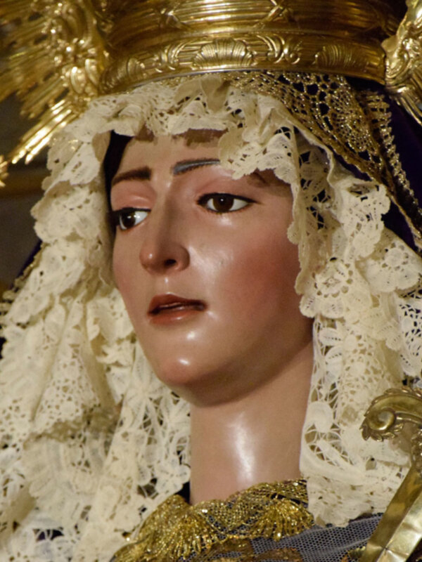 Estatua religiosa con vestimentas de oro y encaje blanco, probablemente una imagen de la Virgen María en una procesión religiosa.